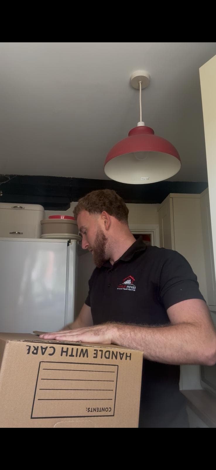 Connor in a Marley Moves branded black polo packing a kitchen item into a Marley Moves cardboard box, the kind of careful step-by-step packing the moving-house checklist walks customers through