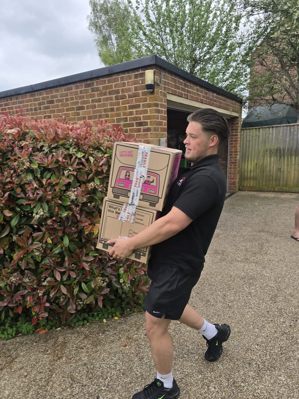 Marley Moves crew member Jack carrying a Marley Moves branded cardboard box up the path of a customer's property, a real day-in-the-life shot from a Dorset removal job